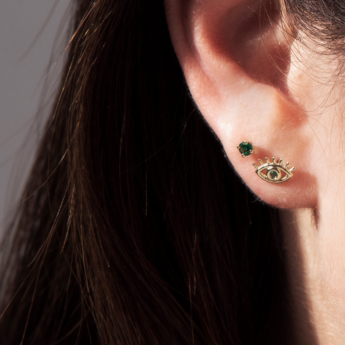 עגילים צמודים מזהב בעיצוב נגד עין הרע משובצים אבני אמרלד